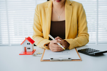 Smiling real estate agent calculating mortgage and presenting house model while sitting at her desk...