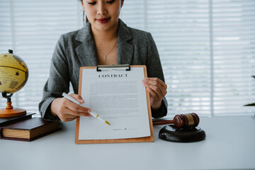 Lawyers discuss a contract on a clipboard, with one pointing to specific terms with a pen, while a...