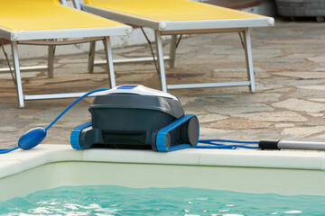 A pool cleaning robot stands at the edge of a pool with clear turquoise water after cleaning....