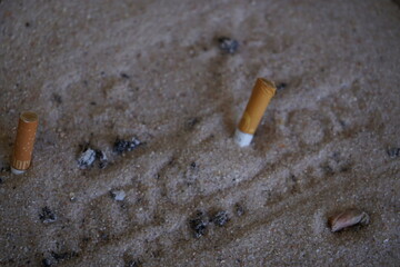 Cigarette butts are partially buried in a sandy surface, surrounded by scattered ash.