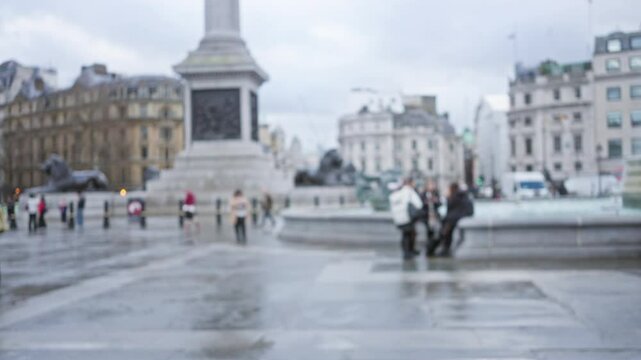 Blurred people in trafalgar square london during winter showing a defocused fountain and historic architecture under a cloudy sky.