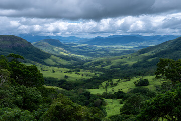 Obraz premium Lush Green Rolling Hills Scenic Valley Landscape View Under Cloudy Sky Distant Mountains Panorama