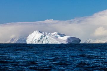 Distant iceberg floating in ocean near the antarctic peninsula. Shoreline in distance; blue water...