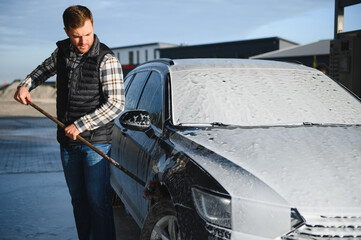 A man washes off the foam while washing the car. A vehicle is engulfed in soapy foam during a car...