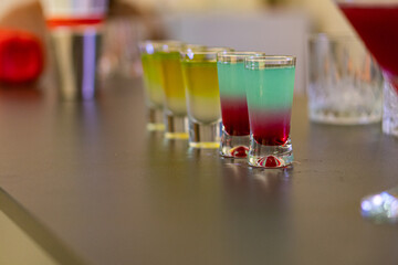 A well-arranged row of martinis, each with a layered gradient color scheme, in a stylish bar setting