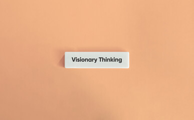 The phrase "Visionary thinking" displayed on a sleek, wide letter tile set against a soft pink background.