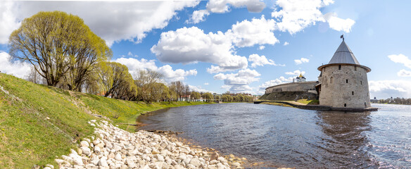 Panoramic view of Pskova River mouth: green slopes with spring foliage, facing Pskov Kremlin walls...