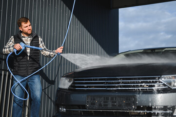 A man washes his car at a self service car wash using a hose with pressurized water.