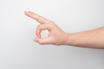 Naklejka premium Close-up of an arm with visible muscle, making a thumbs up gesture against a plain white or off-white background.