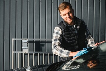 A man wipes his car with a microfiber towel after washing it at a car wash