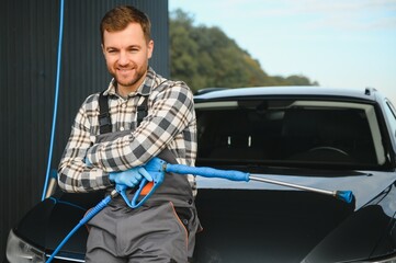 Portrait of a car wash station worker holding a water jet gun next to a clean car
