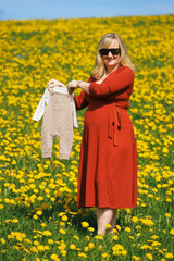 A pregnant woman in a red dress holds newborn baby clothes over her belly, expressing joy and anticipation for her pregnancy and the upcoming birth—perfect for maternity, family, and celebration theme