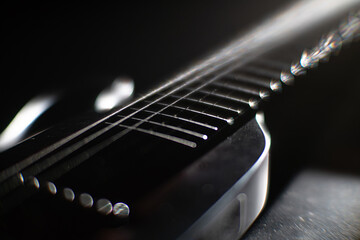 Close-up view of a darkened acoustic guitar with steel strings, emphasizing strings curves and...