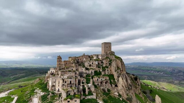 Aerial view of an ancient, abandoned hilltop village of Craco, Italy with stone ruins and a tower.