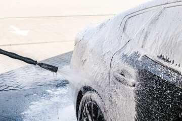 Driver washing car with contactless high pressure water jet,equipment pump in self service car wash.Vehicle covered with foam chemical detergents