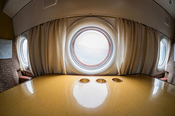Interior of a first-class aircraft cabin, featuring soft lighting, wooden desk with empty seats,...