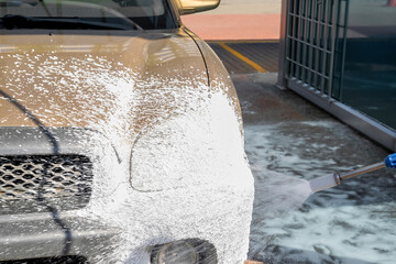 Driver washing car with contactless high pressure water jet,equipment pump in self service car wash.Vehicle covered with foam chemical detergents