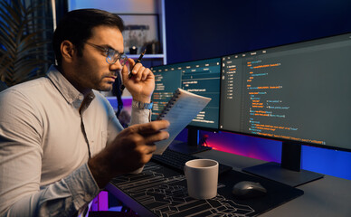 Smart IT developer working on software development coding on pc screen and reading note of newest...