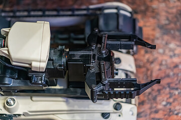 Close-up view of a metallic, mechanical device, with gray, black, and silver tones, in an office or workshop setting, under artificial lighting, no text or people present