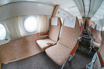 Inside of a daytime passenger aircraft, perspective from cockpit door towards front, beige seats...
