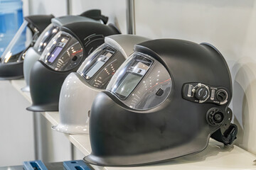 Row of varied helmets with face shields on a display stand, displayed against a shadowed backdrop...