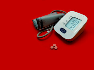 Digital blood pressure monitor with small pink tablets are arranged in a line