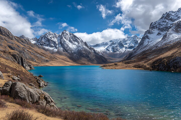 Obraz premium Vibrant Blue Alpine Lake Surrounded by Snowcapped Mountains and Golden Brown Hills under a Sunny Sky
