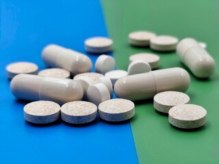 Closeup view of assorted white capsules and round tablets on split blue and green background,...