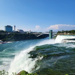 Panoramic view of Niagara Falls with Rainbow Bridge and city skyline under clear blue sky