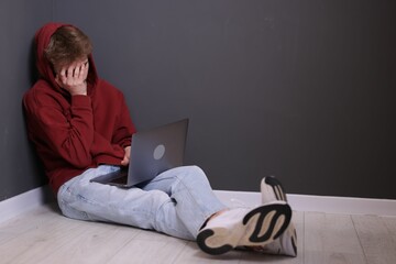 Cyber bullying. Upset teenage boy with laptop on floor indoors. Space for text