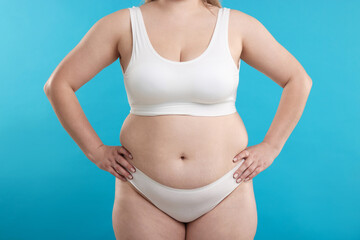 Weight loss. Plus size woman in underwear on light blue background, closeup