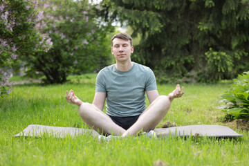 Young man practicing yoga on mat in park