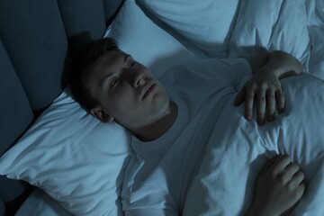 Frustrated man suffering from insomnia in bed indoors, above view