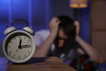 Frustrated man suffering from insomnia indoors, focus on alarm clock