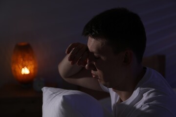 Frustrated man with pillow suffering from insomnia indoors, space for text