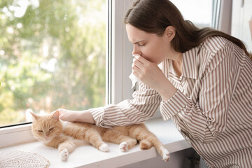 Woman suffering from allergy with her cat near window at home