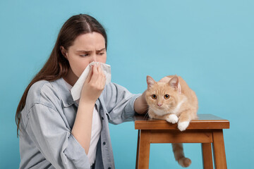 Woman suffering from allergy with her cat on light blue background