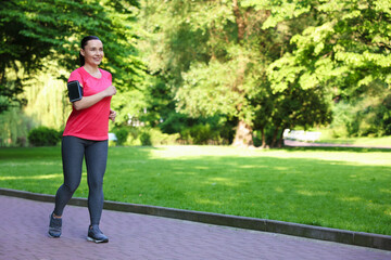 Sporty woman with armband running in park, space for text