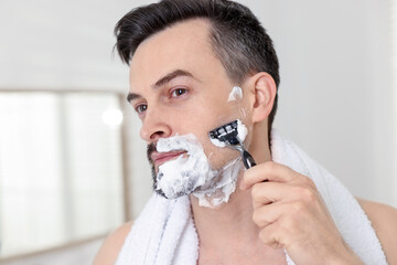 Handsome man shaving with razor at home, closeup