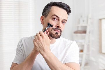 Handsome man shaving with razor at home