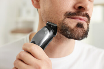 Man shaving with trimmer at home, closeup