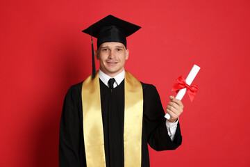 Happy student with diploma after graduation on red background
