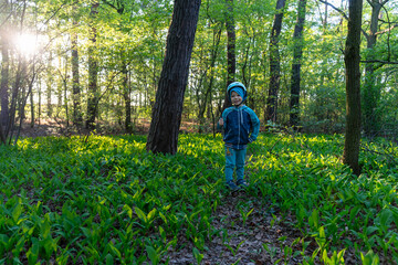 Child in protective helmet enjoying forest walk at golden hour, surrounded by wild green plants and...