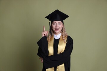 Happy student pointing upwards after graduation on green background