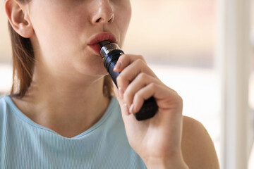 Young woman using electronic smoking device outdoors, closeup