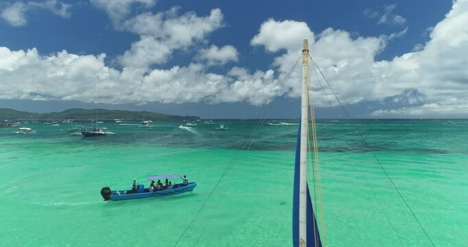 Turquoise tropical sea washing White Beach on Boracay Island, Philippines, with a paraw sailboat resting on the shore and a motorboat carrying tourists in the background