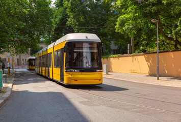 Modern yellow tram on a quiet street with trees in Berlin Germany during summer