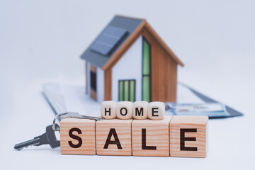 Real estate concept featuring wooden blocks spelling HOME SALE, a keychain with house keys, and a miniature model home with solar panels. Concept property selling and home buying.