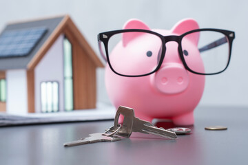 Real estate. Financial concept for home savings, mortgage and real estate investment. Concept with pink piggy bank with glasses a miniature eco-friendly house model with solar panels, keys, and coins.