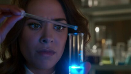 A female scientist carefully drops liquid into a glowing test tube, her eyes reflecting the blue chemical light, captured in a vivid close-up in the lab - Powered by Adobe